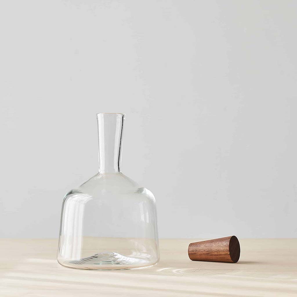 A Michael Ruh hand blown glass bottle filled , featuring a wooden stopper, displayed in a still life composition.